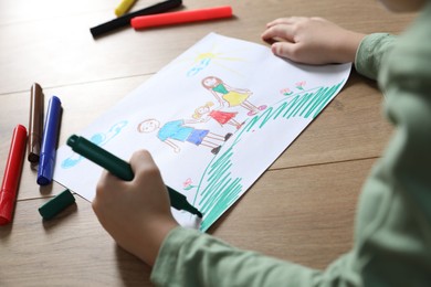 Photo of Little boy drawing picture with marker at wooden table, closeup. Child`s art