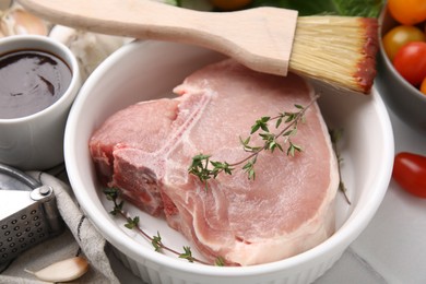 Photo of Raw meat, thyme and brush with marinade on light table, closeup