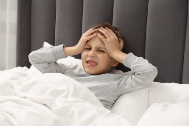 Photo of Little boy suffering from headache in bed at home