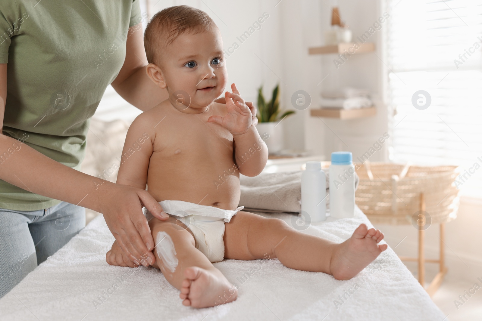 Photo of Mother applying body cream on her little baby at home, closeup