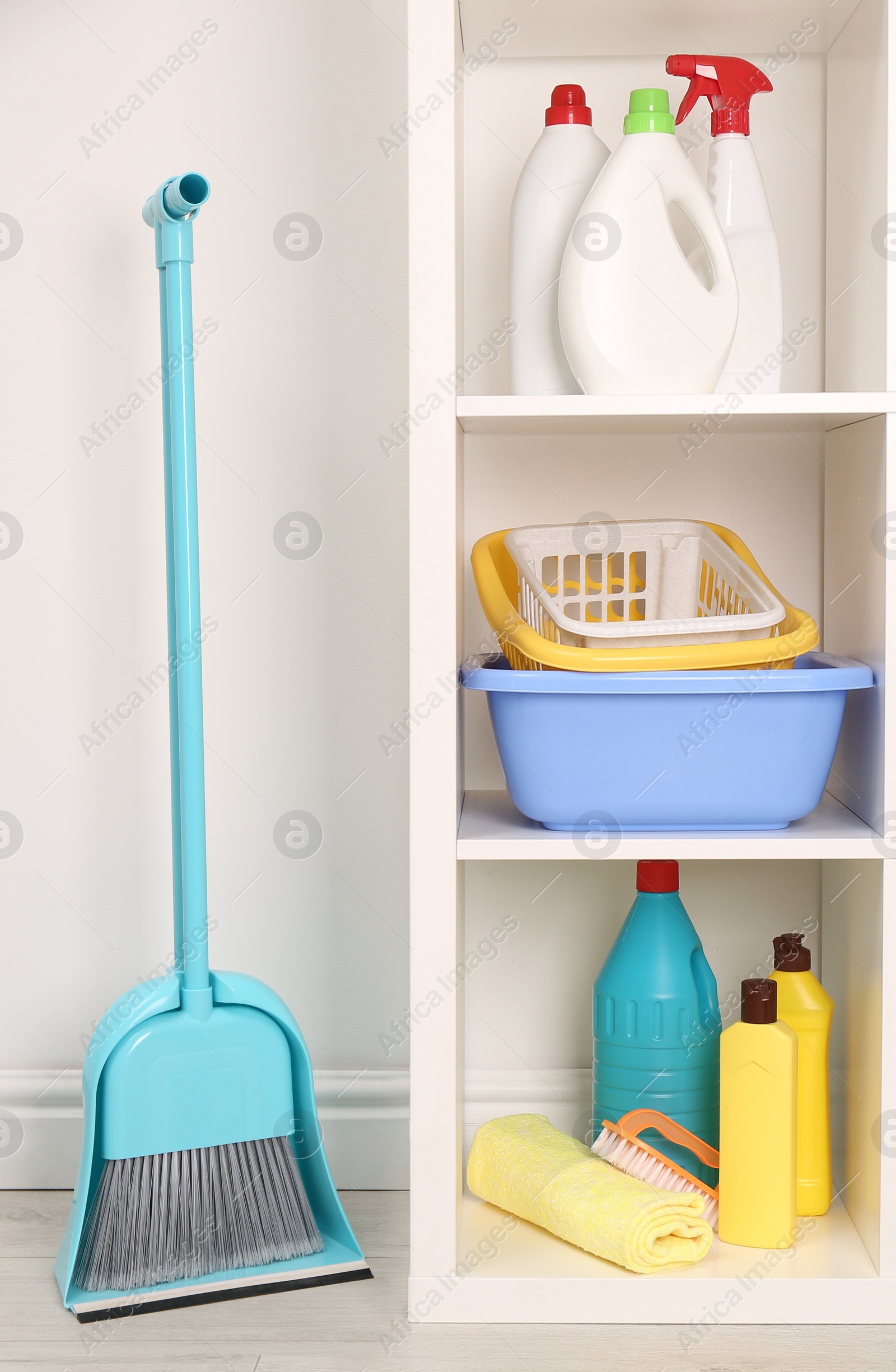 Photo of Shelving unit with detergents and cleaning tools near white wall indoors