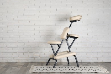 Photo of Modern massage chair near white brick wall indoors, space for text. Medical equipment