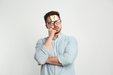 Photo of Pensive man with question mark sticker on forehead against light background