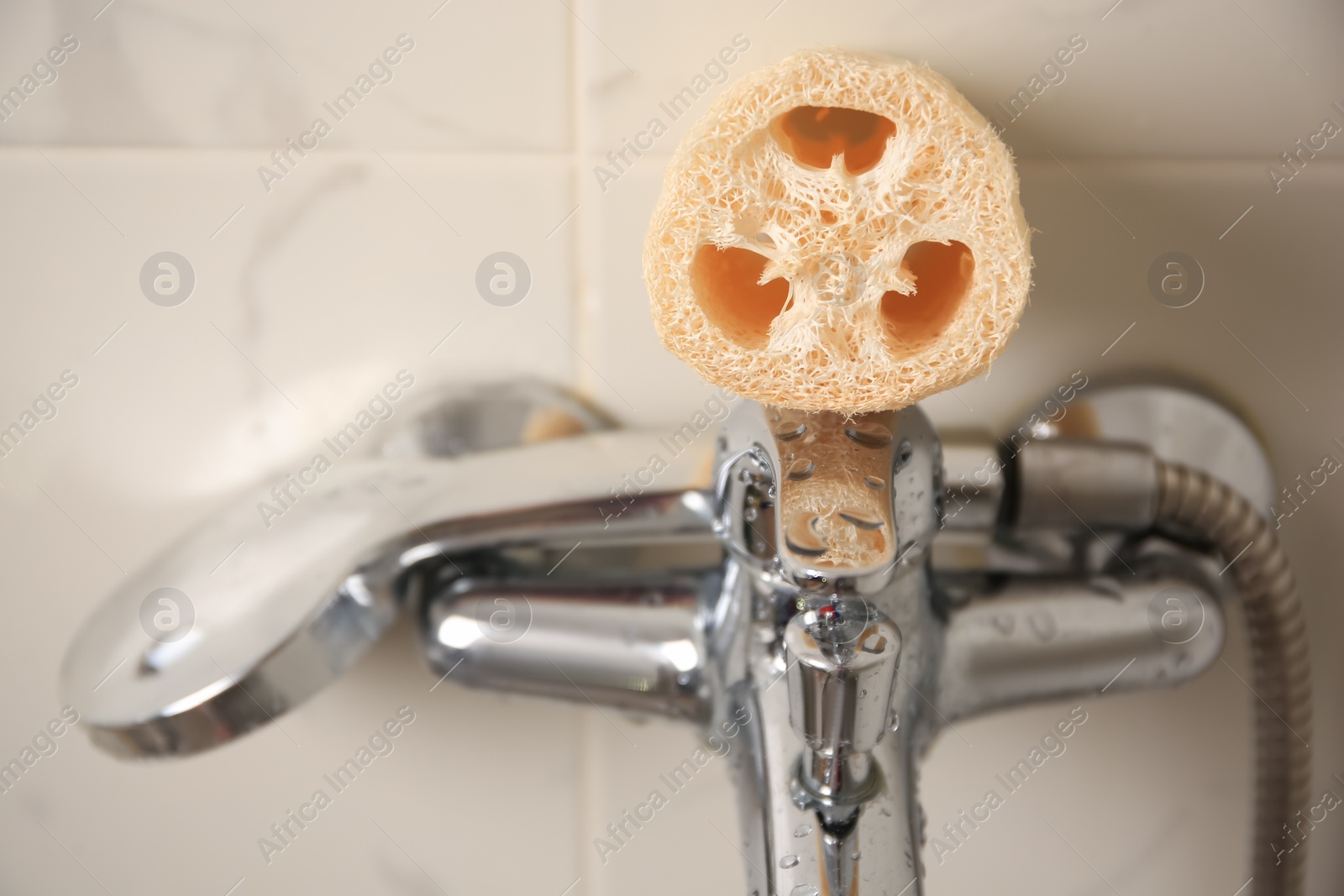 Photo of Natural loofah sponge on faucet in bathroom, closeup