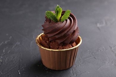 Delicious chocolate cupcake with mint on black textured table, closeup