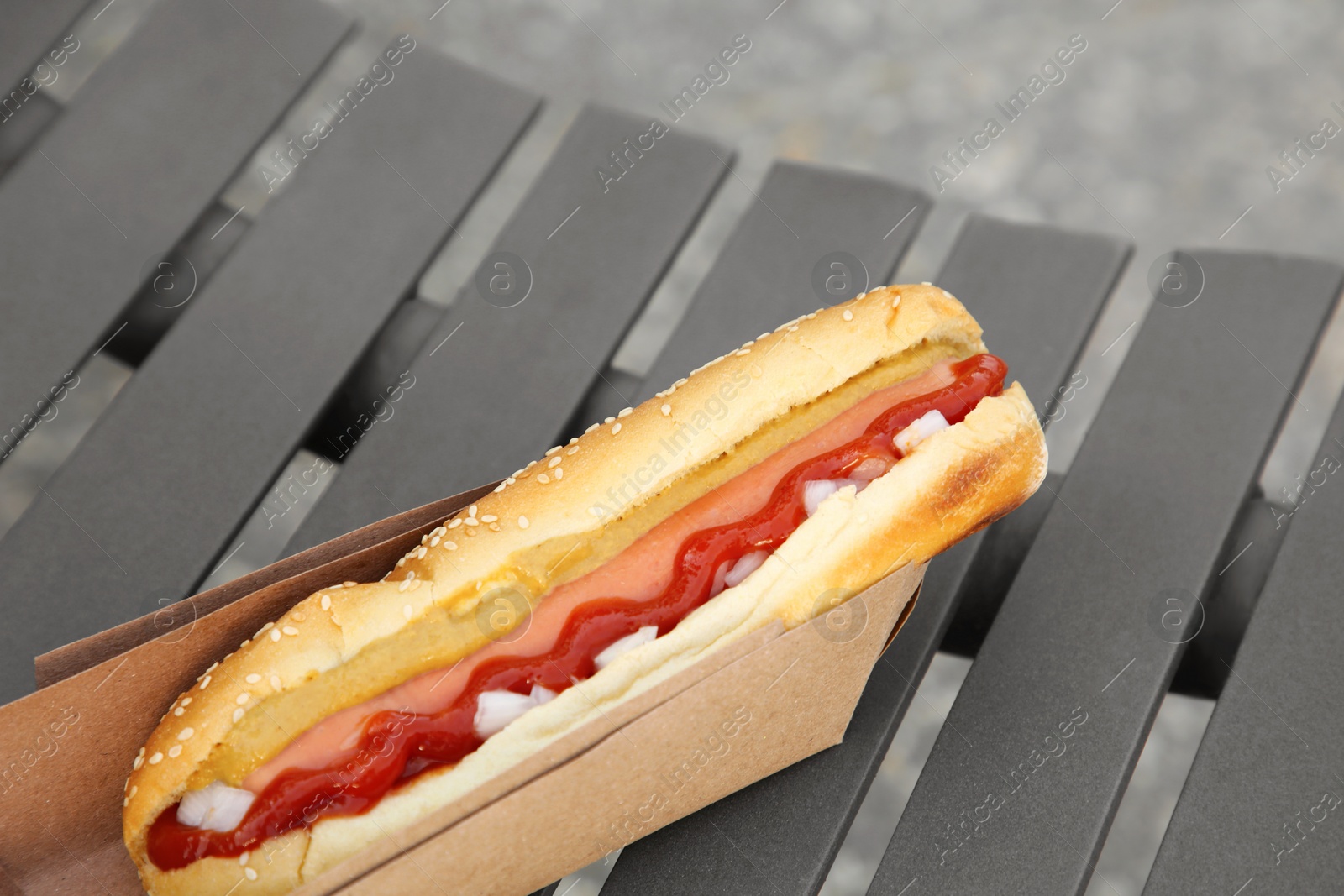 Photo of Fresh delicious hot dog with sauce on black bench outdoors