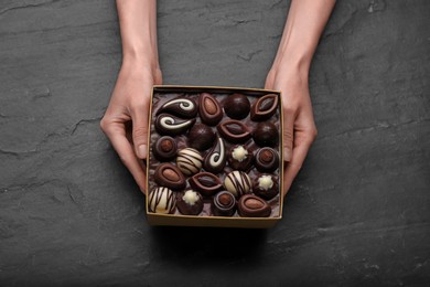 Woman with box of delicious chocolate candies at black table, top view