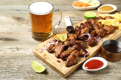 Photo of Tasty roasted chicken wings served with beer on wooden table. Space for text