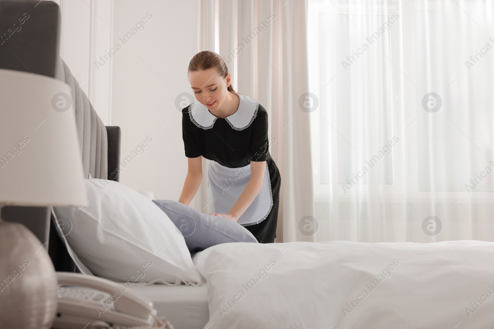 Photo of Young maid making bed in hotel room. Space for text