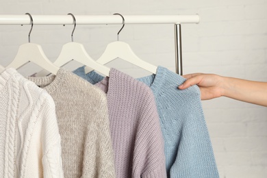 Woman choosing sweater on rack against brick wall