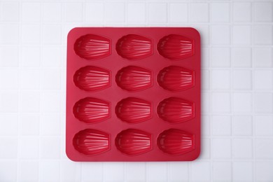 Red baking mold for madeleine cookies on white tiled table, top view