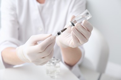 Photo of Doctor filling syringe with medication from vial on blurred background, closeup