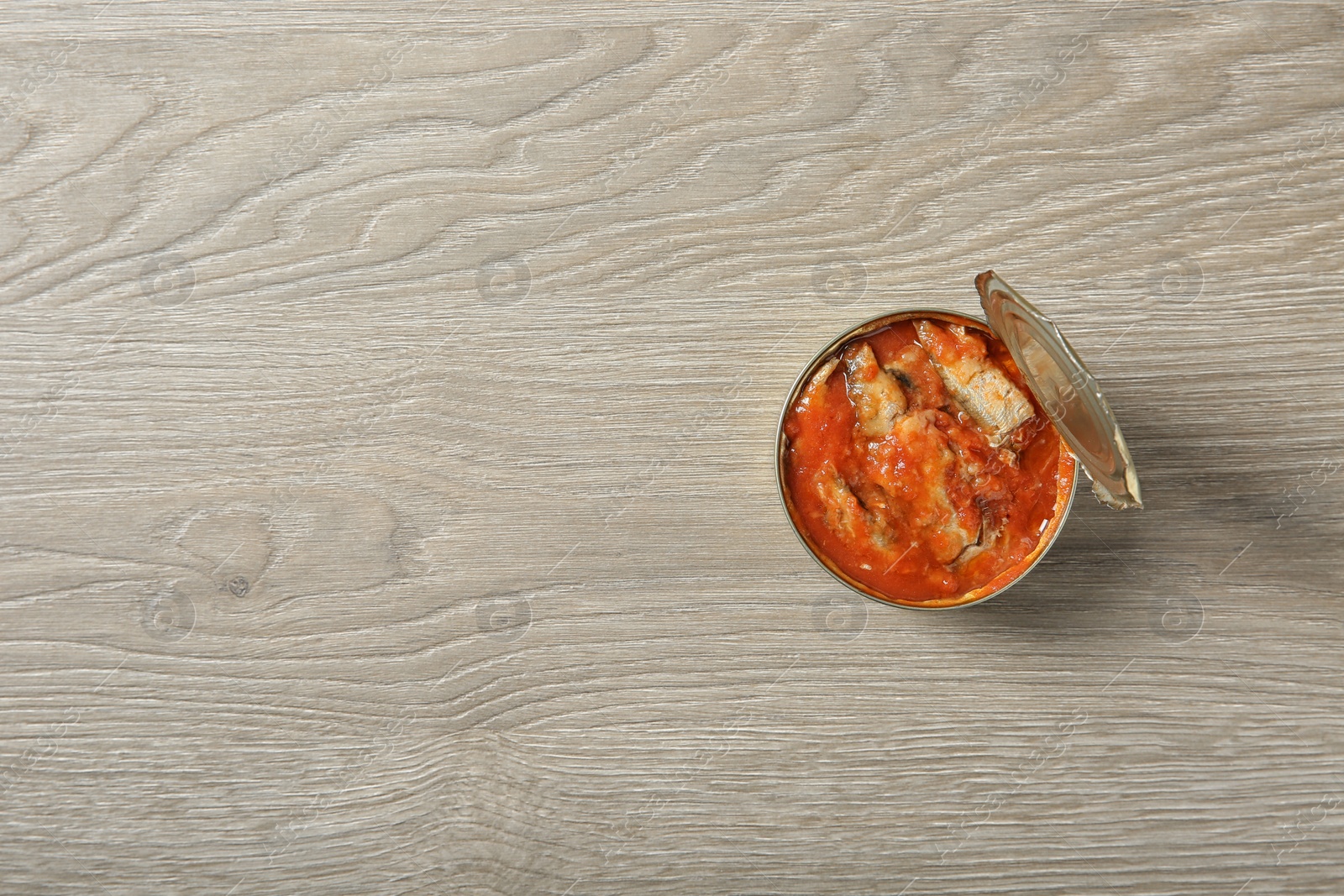 Photo of Open tin can of fish in tomato sauce on wooden background, top view. Space for text
