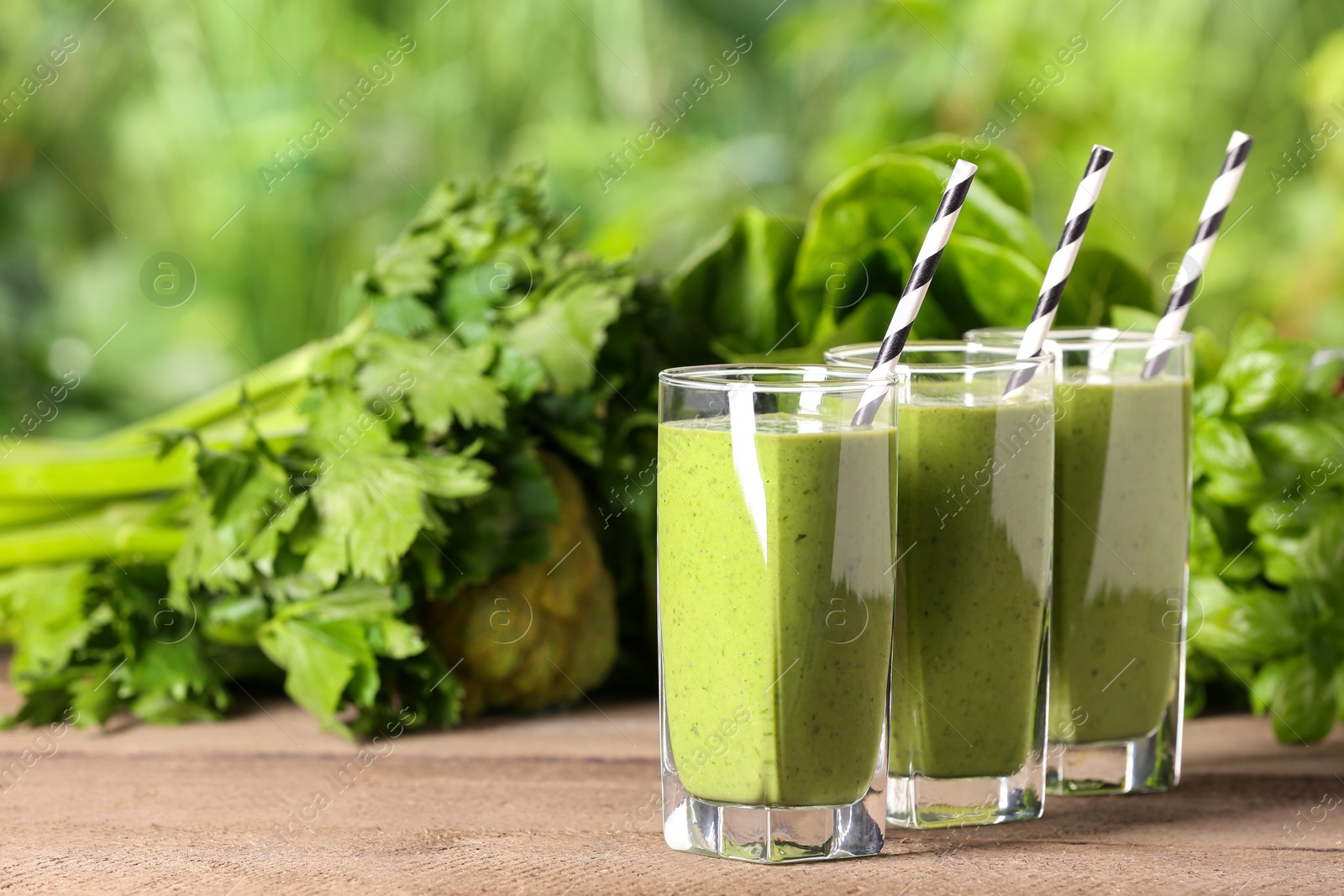 Photo of Glasses of fresh green smoothie and ingredients on wooden table outdoors, space for text