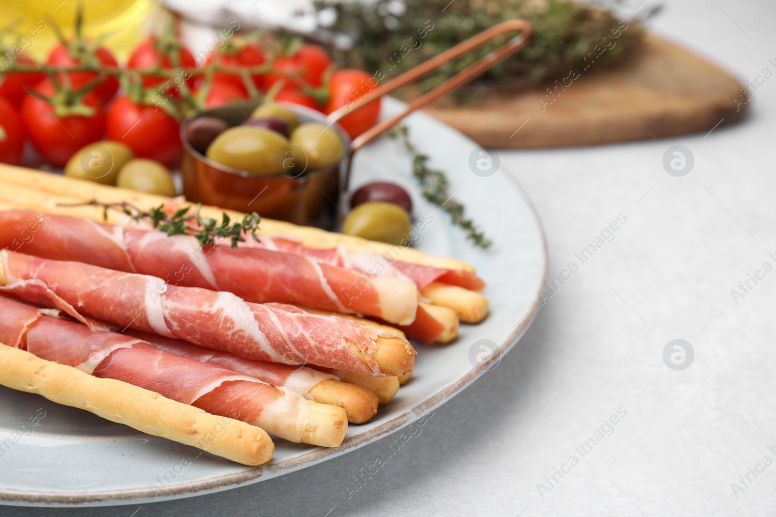 Photo of Delicious grissini sticks with prosciutto and snacks on white table, closeup