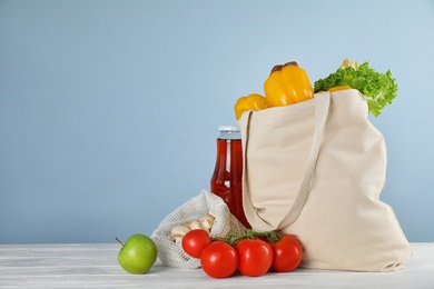 Shopping bag with fresh vegetables and other products on white wooden table against light blue background, space for text