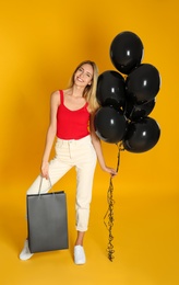 Happy young woman with balloons and shopping bag on yellow background. Black Friday Sale