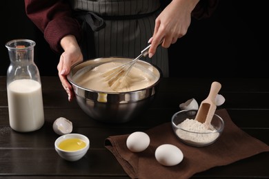 Woman making dough with whisk in bowl at table, closeup