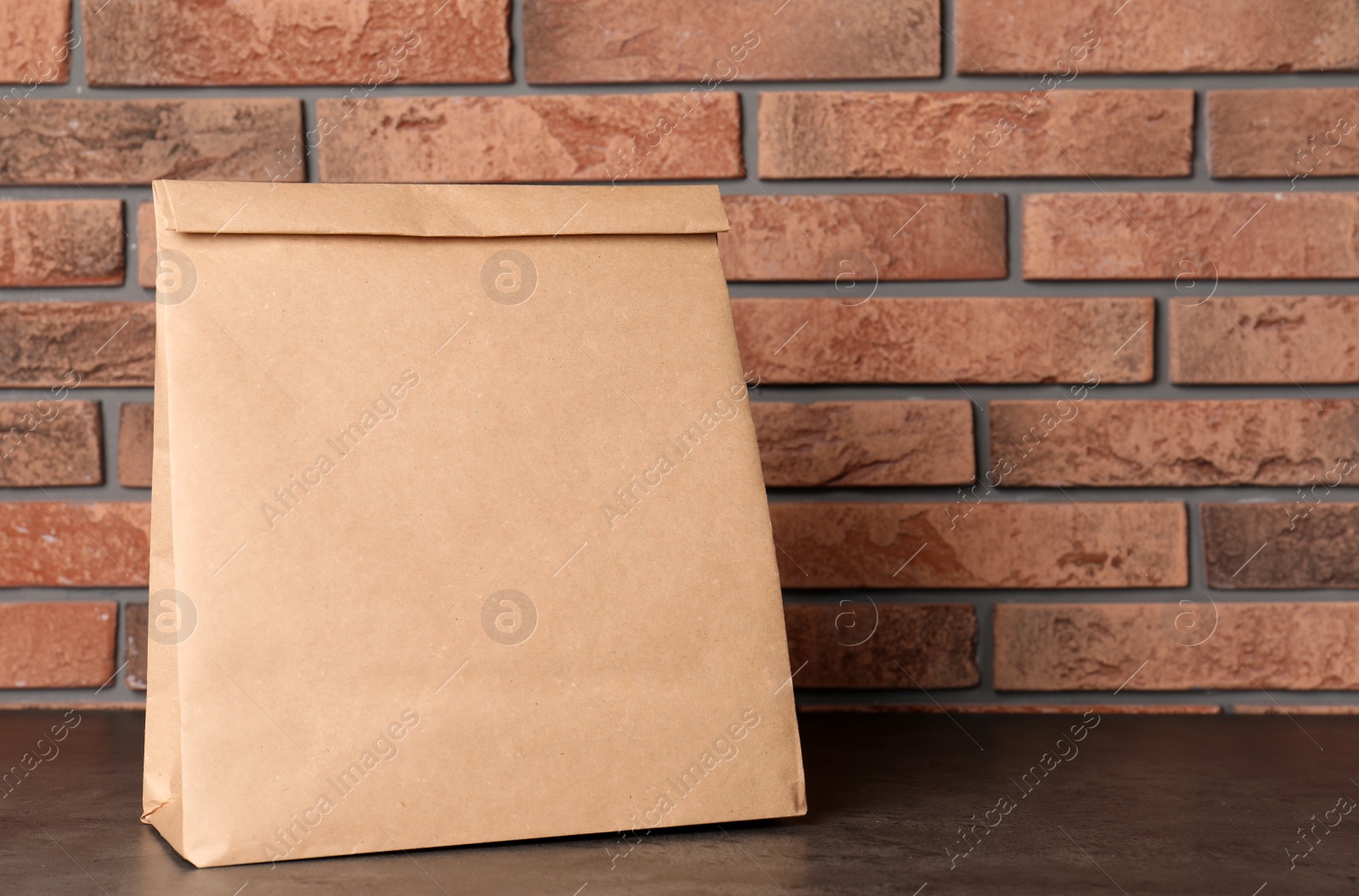 Photo of Paper bag on table against brick wall. Mockup for design