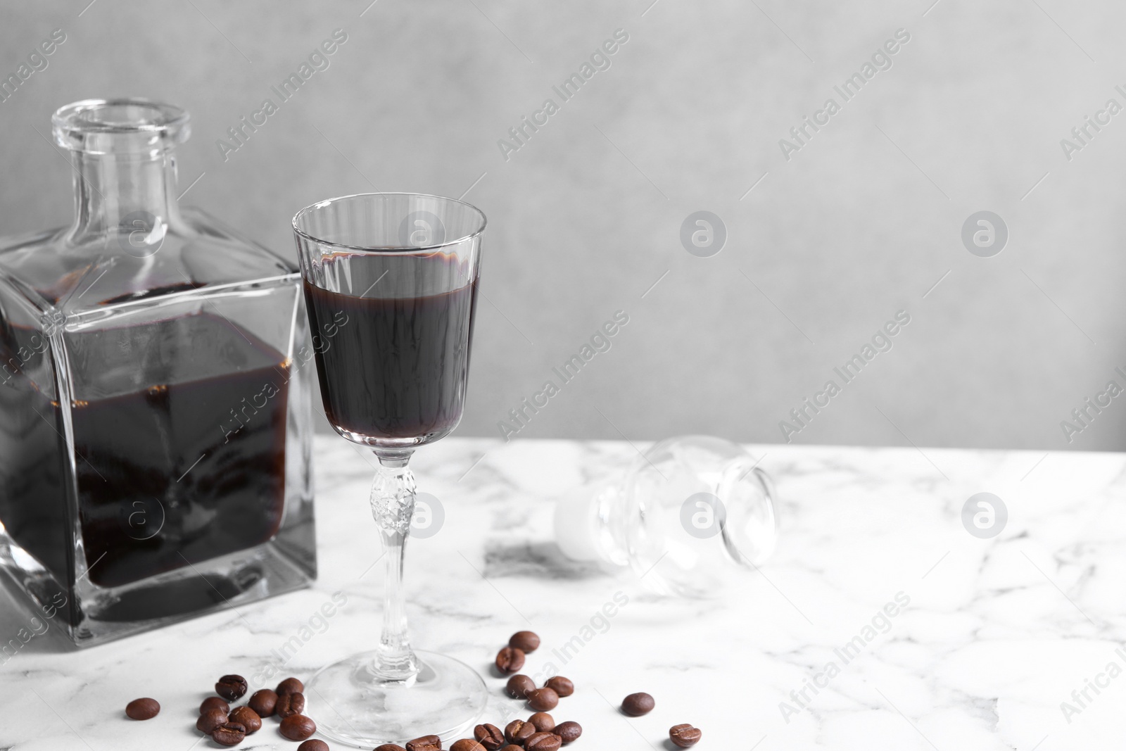 Photo of Coffee liqueur and beans on white marble table. Space for text