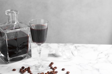 Photo of Coffee liqueur and beans on white marble table. Space for text