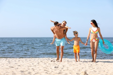 Happy family with inflatable ring on sandy beach near sea. Summer holidays