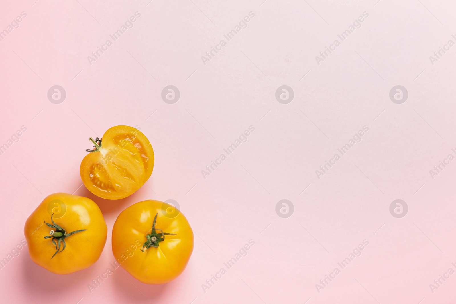 Photo of Cut and whole ripe yellow tomatoes on pink background, flat lay. Space for text