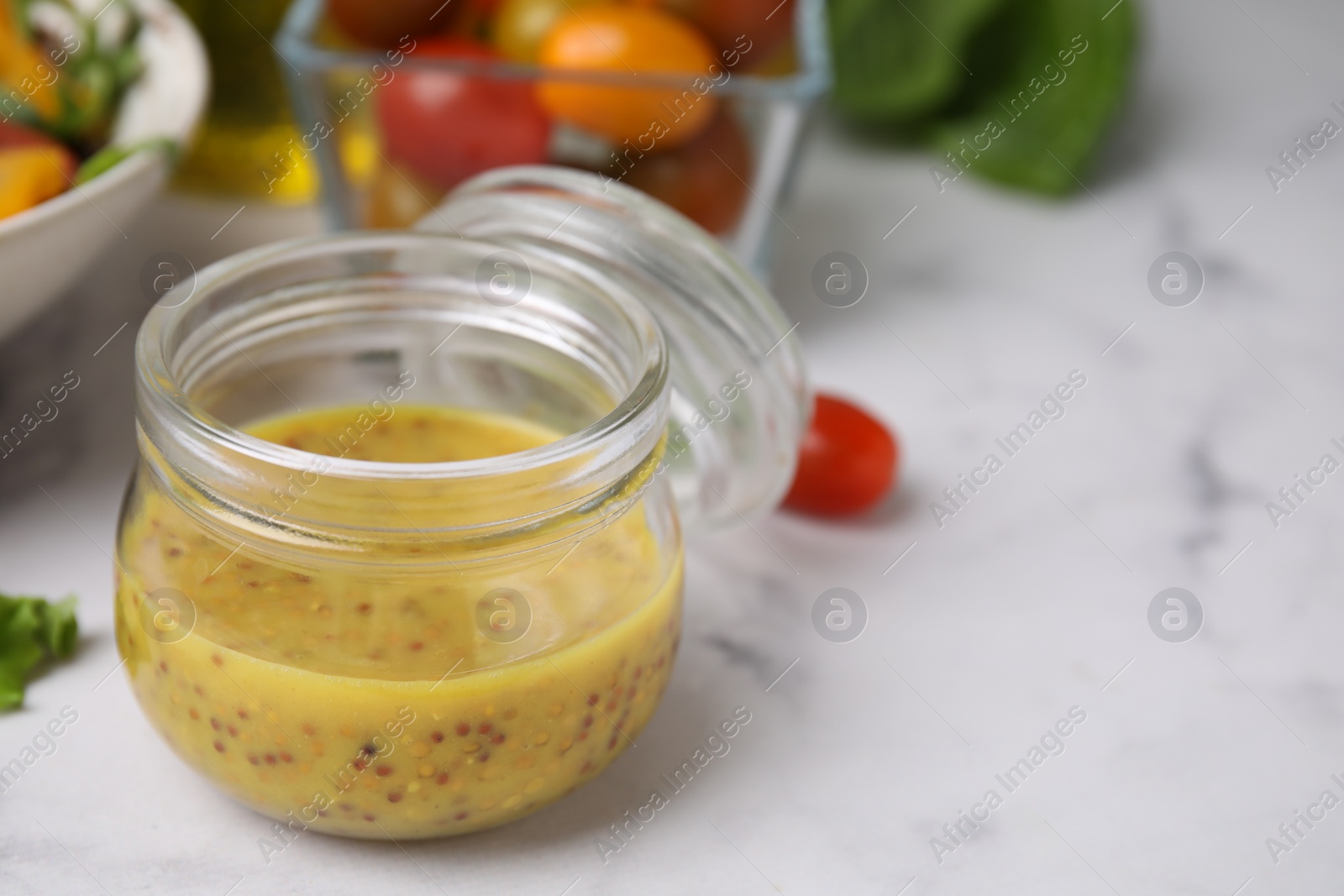 Photo of Tasty vinegar based sauce (Vinaigrette) in jar on white marble table, closeup. Space for text