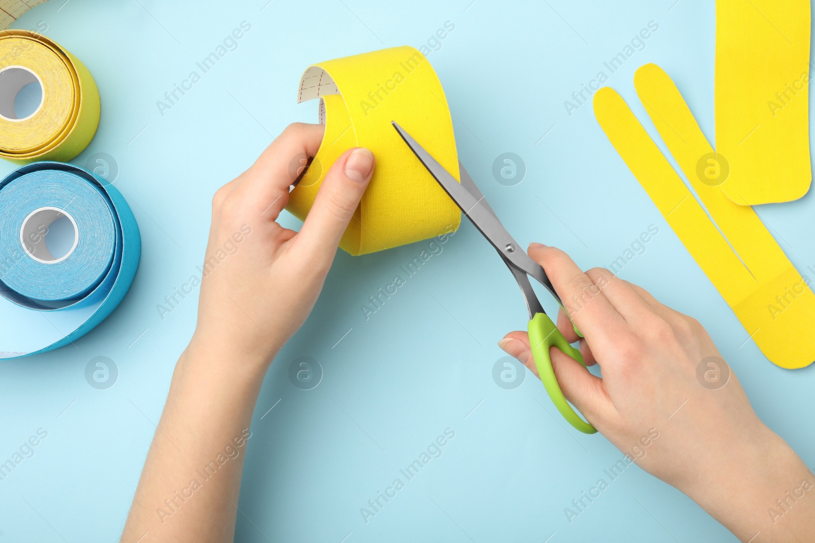 Photo of Woman cutting bright kinesio tape at light blue table, top view