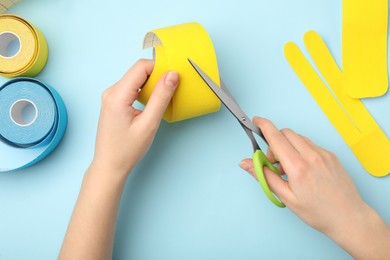 Woman cutting bright kinesio tape at light blue table, top view