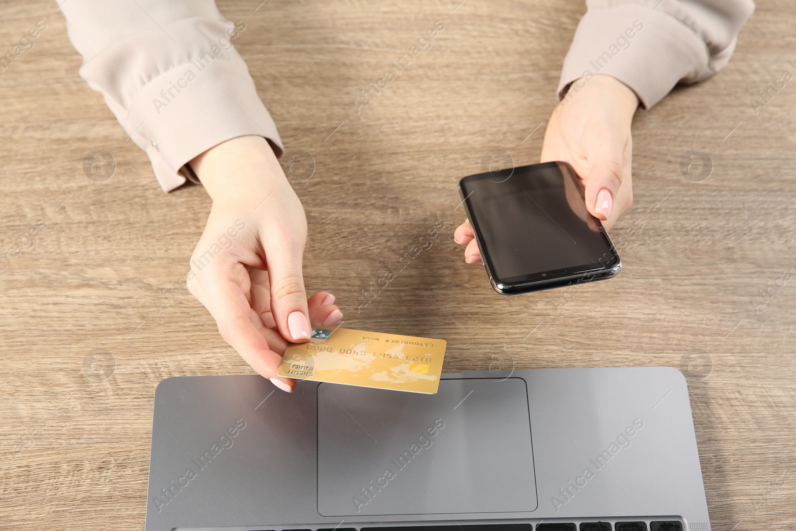 Photo of Online payment. Woman using credit card and smartphone near laptop at wooden table, top view