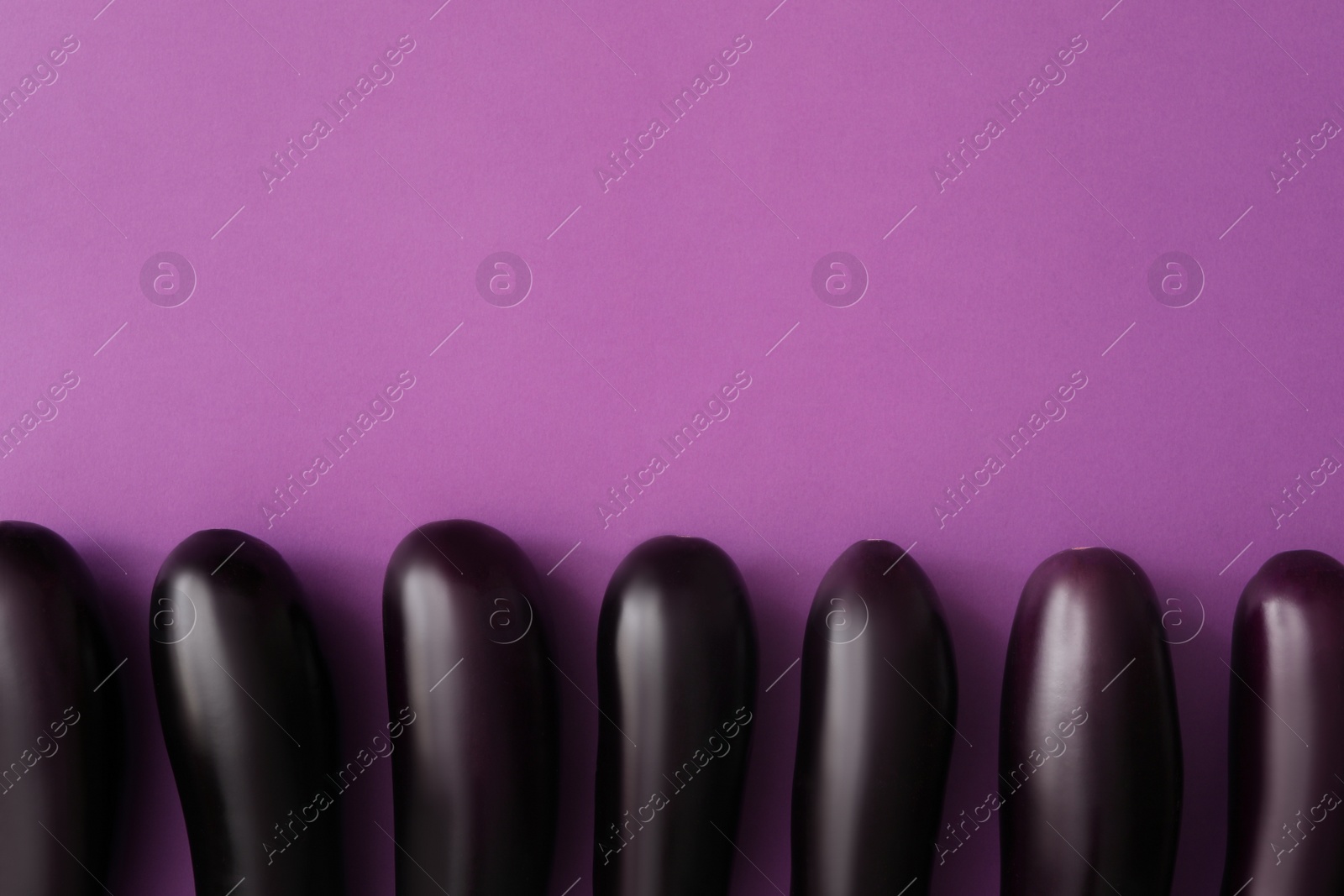 Photo of Raw ripe eggplants on purple background, flat lay. Space for text