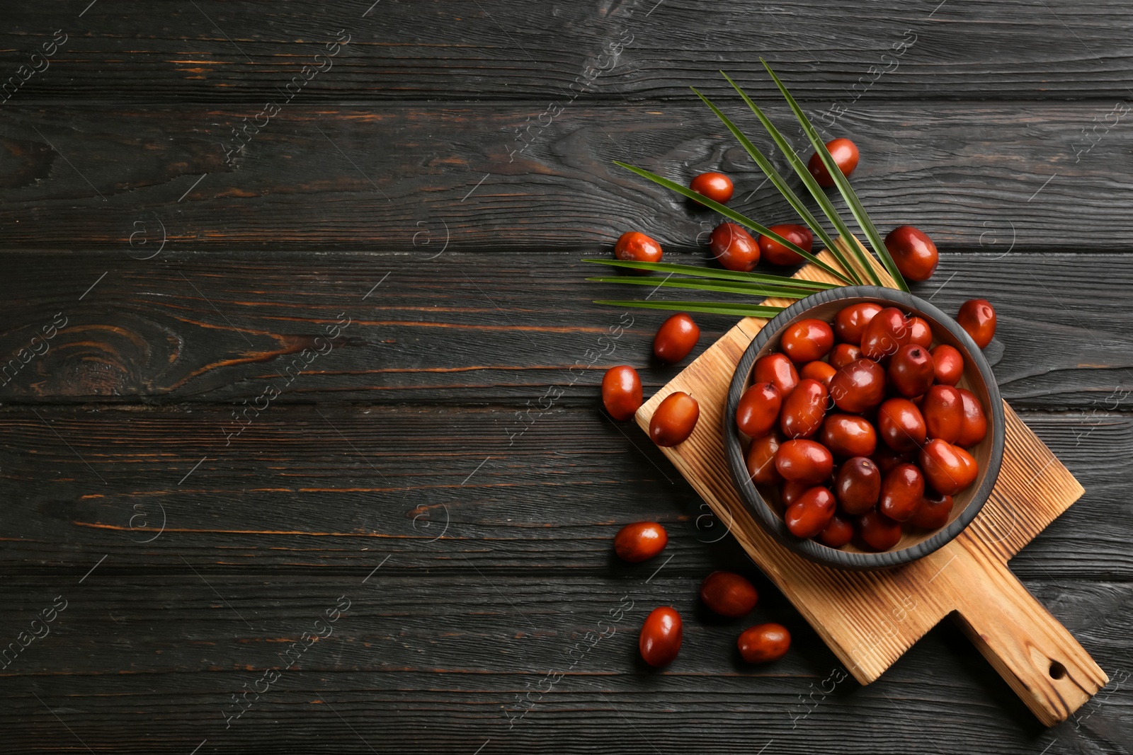 Photo of Palm oil fruits in bowl on black wooden table, flat lay. Space for text