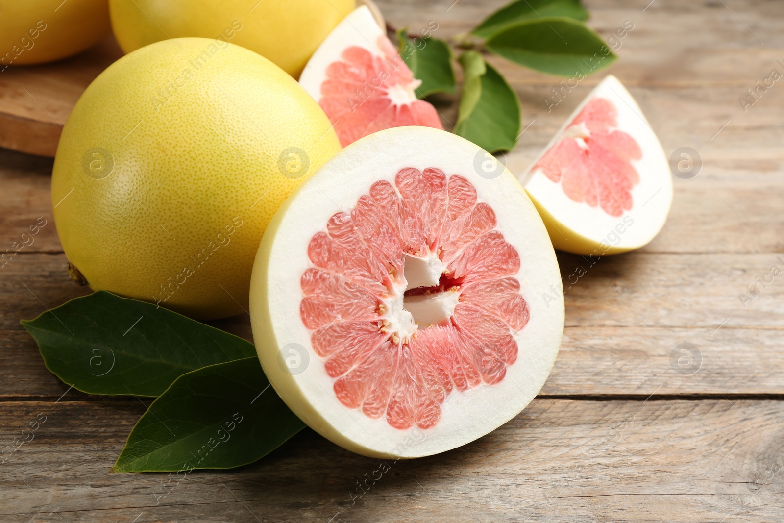 Photo of Fresh cut and whole pomelo fruits on wooden table, closeup