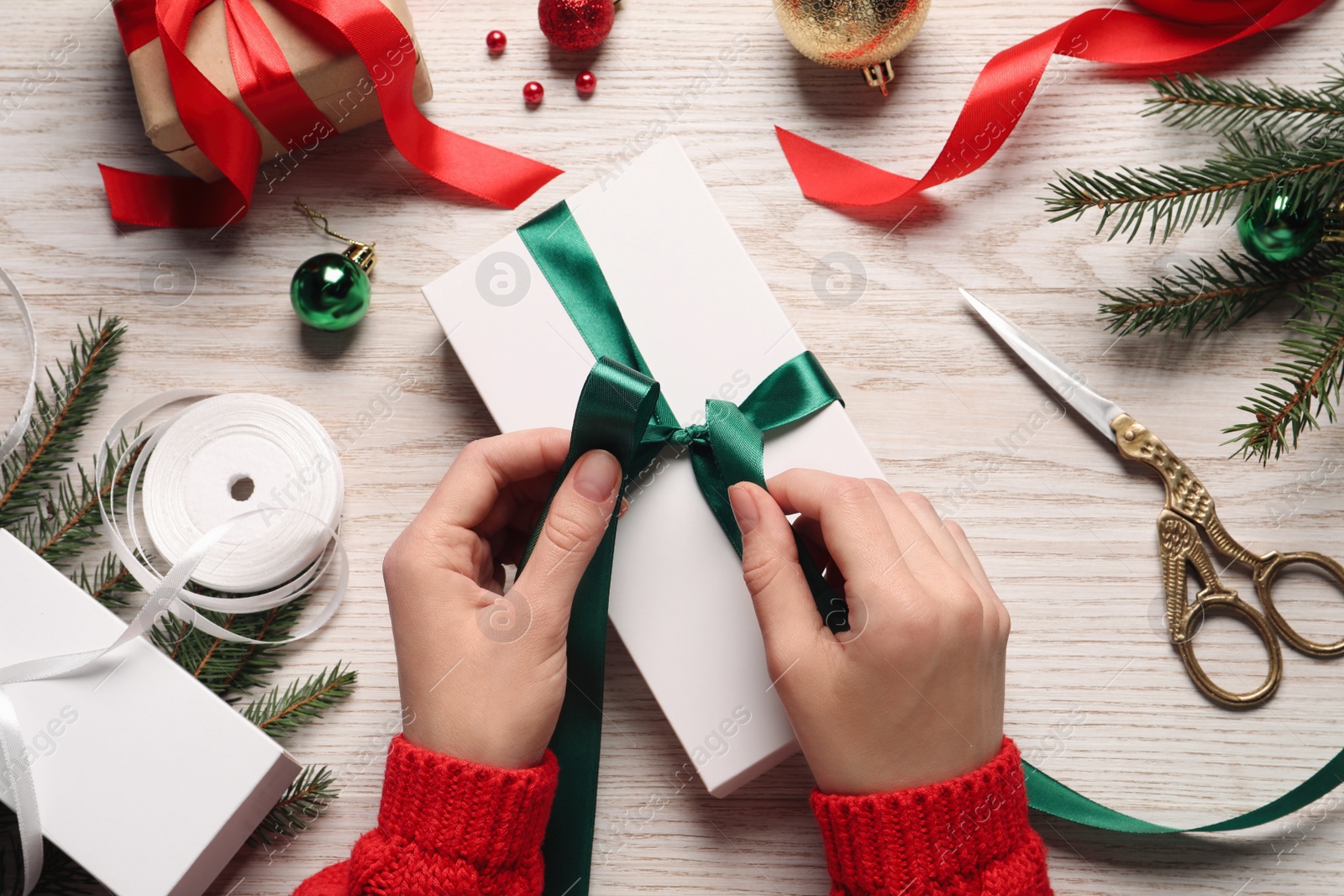 Photo of Woman decorating gift box at white wooden table, top view. Christmas present