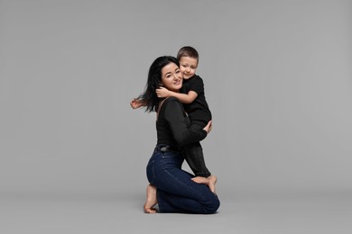 Beautiful mother hugging little son on grey background