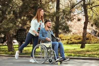 Photo of Young man in wheelchair and joyful woman at park