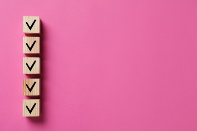 Image of Wooden cubes with check marks on pink background, top view. Space for text