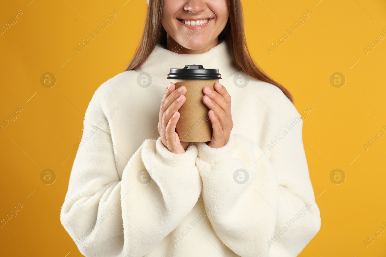 Photo of Happy beautiful woman with paper cup of mulled wine on yellow background, closeup