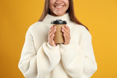 Happy beautiful woman with paper cup of mulled wine on yellow background, closeup