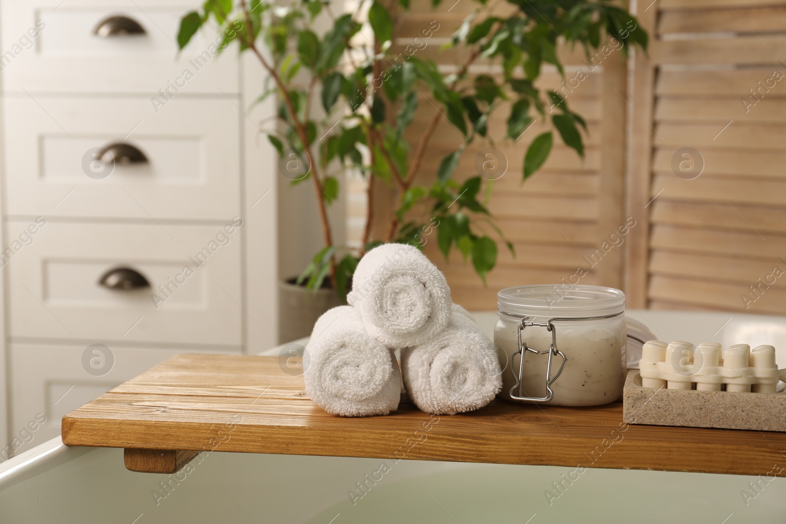 Photo of Wooden tray with spa products and towels on bath tub in bathroom. Space for text