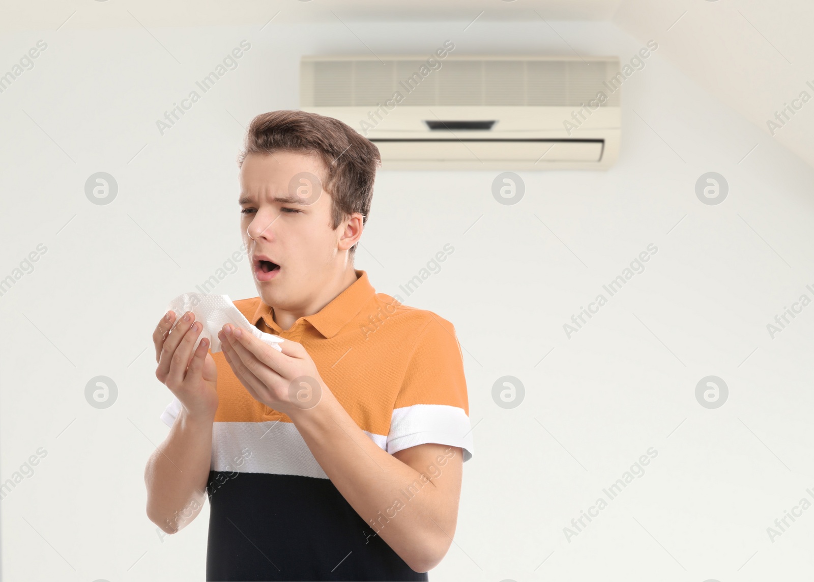 Image of Boy suffering from cold in room with air conditioner on white wall