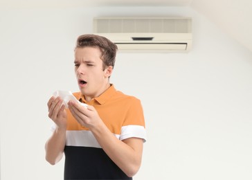 Image of Boy suffering from cold in room with air conditioner on white wall