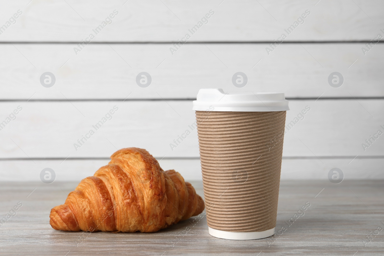 Photo of Coffee to go. Paper cup with tasty drink and croissant on white wooden table