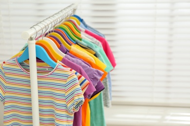 Different child's clothes hanging on rack indoors. Space for text