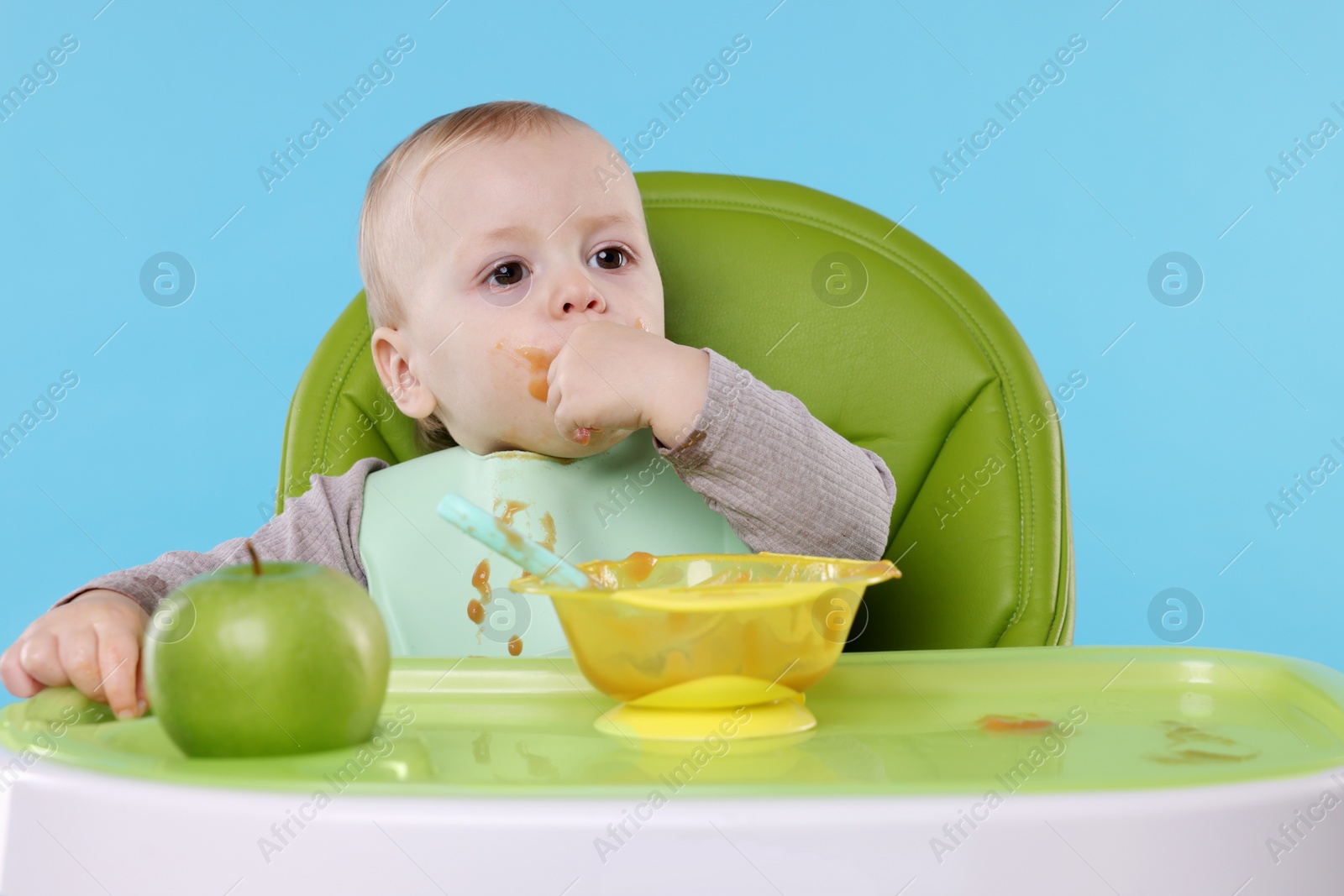 Photo of Cute little baby eating healthy food in high chair on light blue background