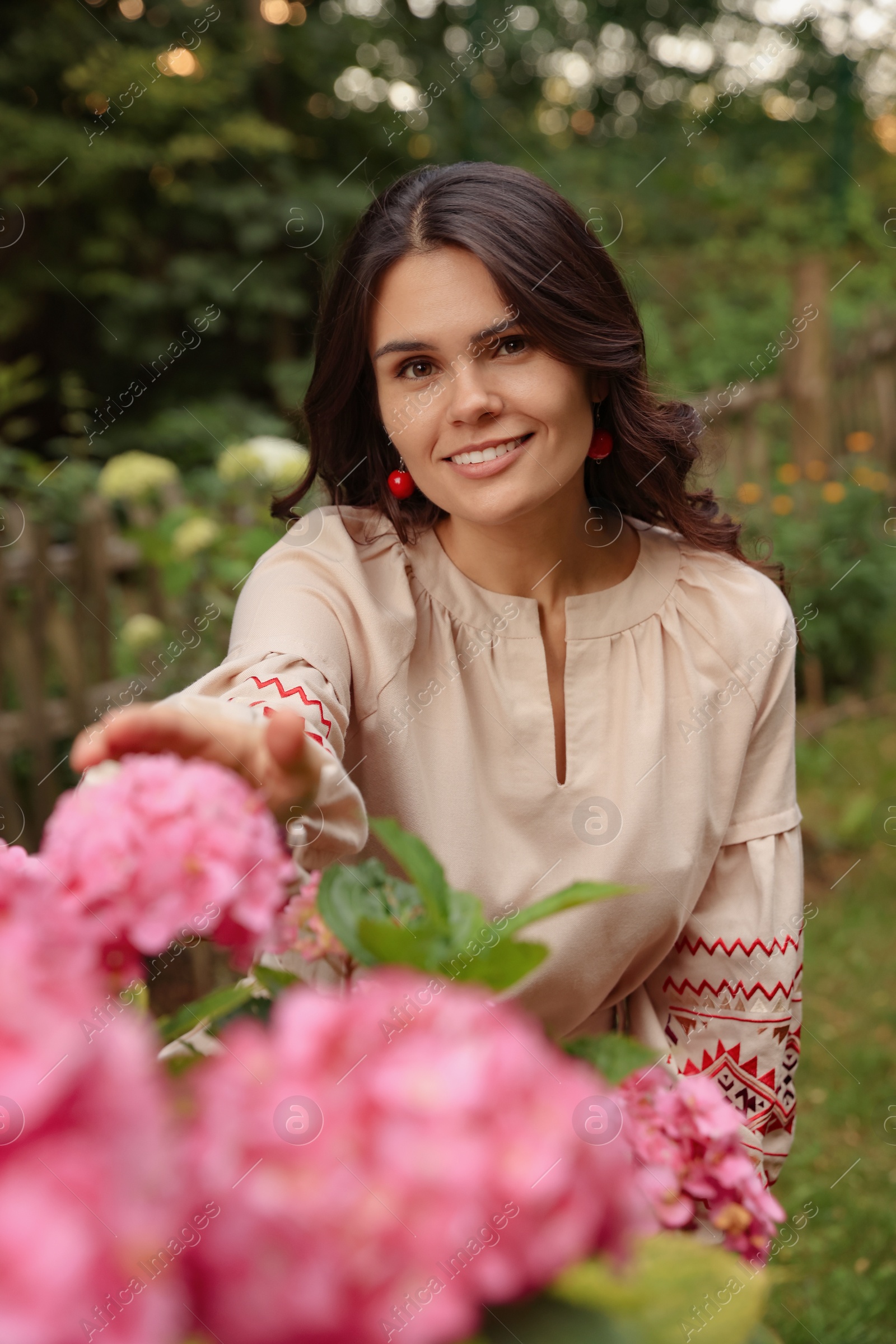 Photo of Beautiful woman wearing embroidered dress in blooming garden. Ukrainian national clothes