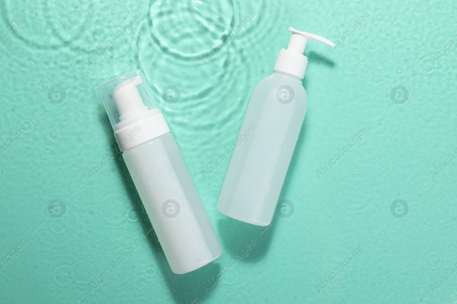 Photo of Bottles of face cleansing product on water against turquoise background, flat lay