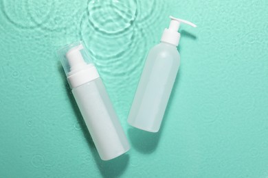 Photo of Bottles of face cleansing product on water against turquoise background, flat lay