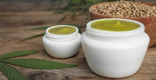 Jars of hemp cream on wooden table against blue background, closeup. Organic cosmetics